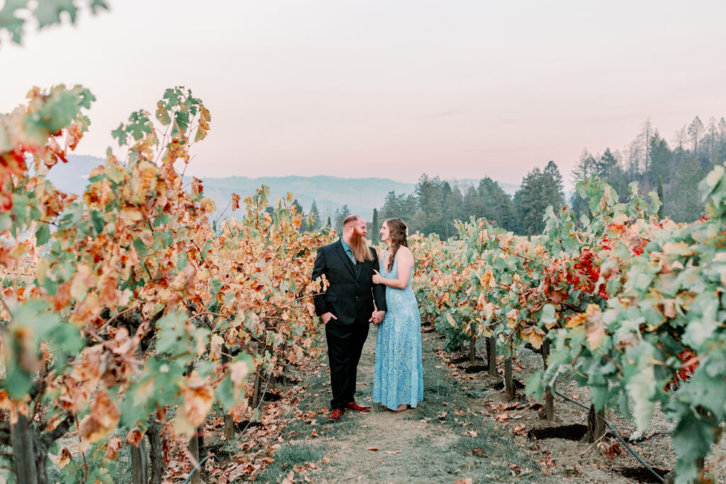 couple walking through a vineyard holding hands and looking at each other during their engagement session at Castello Di Amorosa in Napa Valley California engagement photos by Sarah Schweyer Photography