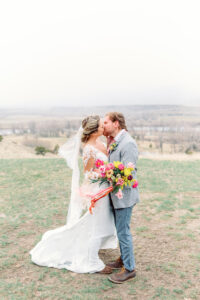 bride and groom kissing on their wedding day with multi colored bouquet at Sage Lodge in Bozeman Montana