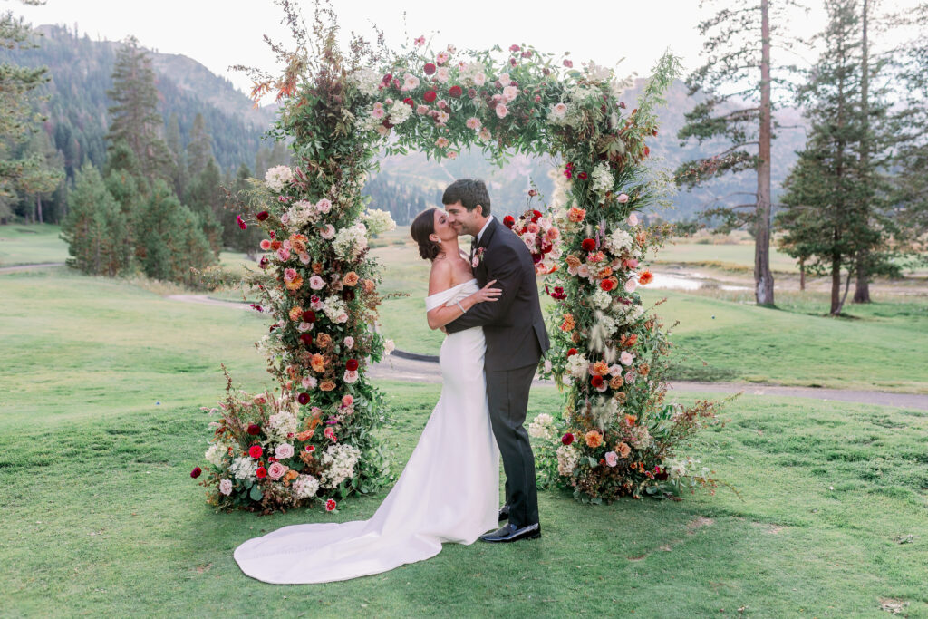 bride and groom under floral arch at their wedding in Tahoe Olympic Valley California with views of the mountains behind them